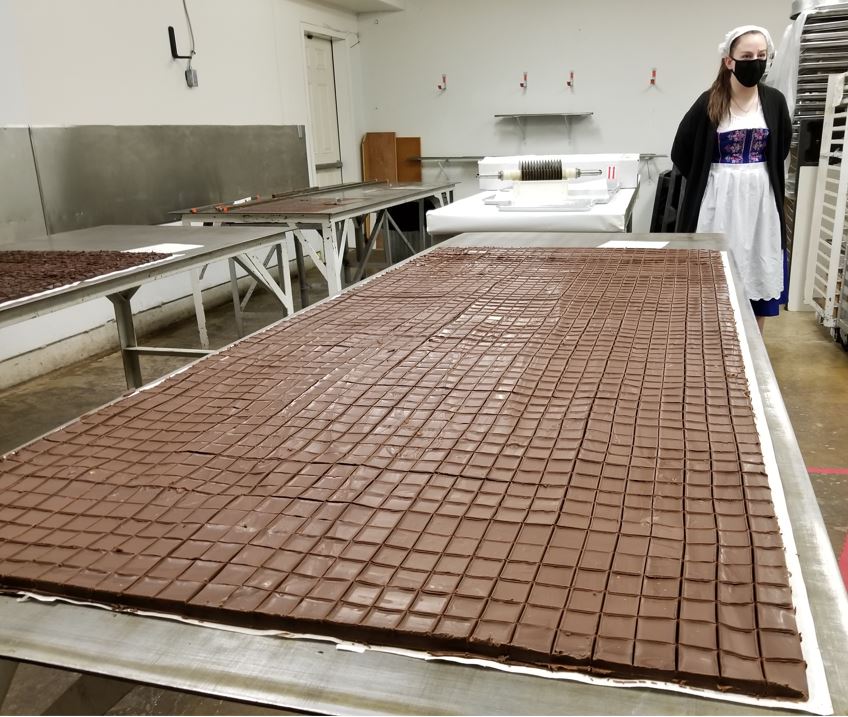 That is one huge sheet of chocolate!   If you look to the back wall you will see the device that is rolled across the sheet in one direction, then in the other, in order to quickly cut it into small bite-size pieces.